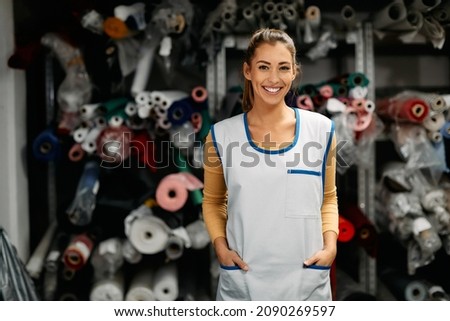 Portrait of happy dressmaker working at clothing workshop and looking at camera.