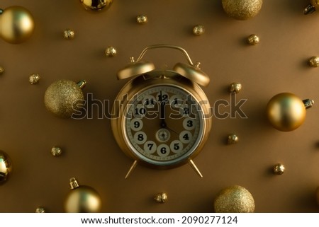 Golden Christmas baubles and vintage alarm clock on gold background. Aesthetic Christmas and New Year ornament concept. Monochromatic retro composition.