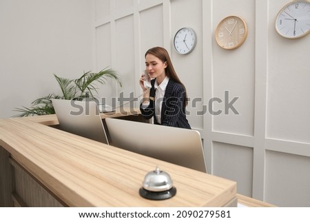 Beautiful receptionist talking on phone at counter in hotel