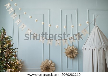 Stylish and cozy nursery with a tent, Christmas tree and hanging cotton flags with the inscription Merry Christmas. Contemporary scanidnavian interior with white wall. children's room decorated for
