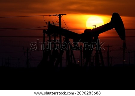 Silhouette of crude oil pump in oilfield at sunset