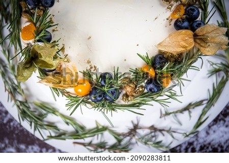 Beautiful chocolate homemade christmas cake on a white stand on a  wooden table. Christmas decoration with rosemary all around. Top view.