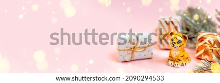 Tiger symbol of the Chinese new year 2022. Figurine of tiger with branches spruce tree and golden gift boxes on pink pastel background. Copy space. Banner