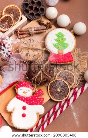 Christmas cozy and beautiful picture with tasty gingerbread and dark chocolate cookies, white round shaped christmas tree decorations, candle, cane candies, orange slices and chinnamon sticks top view
