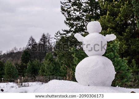 photo of snow on which stands a large snowman. The figure of a snowman in the background of the forest lit by the sun. Sunny day in the winter. Brilliant snow after heavy snowfall.