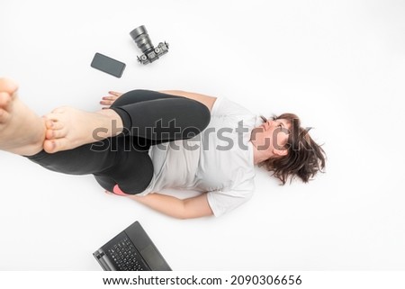 Plus size woman in sportswear surrounded by gadgets. Top view portrait of girl next to laptop, phone and camera on white background