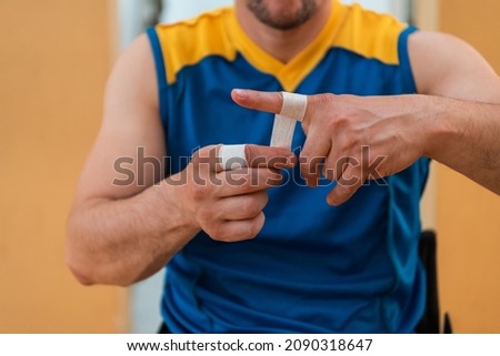 a person with a disability puts on a corset and bandages on his arms and fingers in preparation for a game in the arena