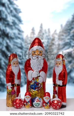 Christmas greeting card. Closeup of various cheerful wrapped chocolate Santa Claus over festive abstract blurred winter landscape. Xmas and New Year gift sweets. Macro.