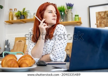 Smiling middle aged woman sitting at the table in her dining room drawing on a tablet computer with a stylus, close up