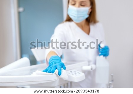 Nurse in protective gloves cleaning work surface at stomatology clinic, sanitizing table with disinfectant spray bottle, washing dental chair with towel, selective focus Royalty-Free Stock Photo #2090343178