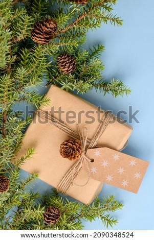 Christmas background with natural fir tree branches, craft gift with tag and pine cones on pastel blue background, winter web banner, close up