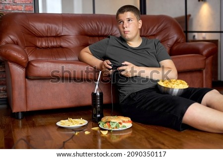 european child boy eating fries. Fast food. Kid and unhealthy lifestyle concept. teenager boy playing console, have rest alone, sitting on floor, eating junk food, hamburgers and crisps on plate