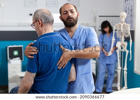 Orthopedic nurse stretching spinal cord and shoulder of elder patient with injury for physiotherapy. Chiropractor giving help to senior man with back pain for physical recovery. Royalty-Free Stock Photo #2090366677