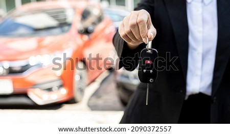 A person holding a car key, a female car rental company employee is about to deliver the car to a customer who has signed a rental contract and paid the deposit. Car rental concept.