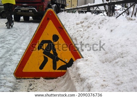 Winter photography with a triangular warning road sign in the snow. Renovation work sign. Digging man icon.