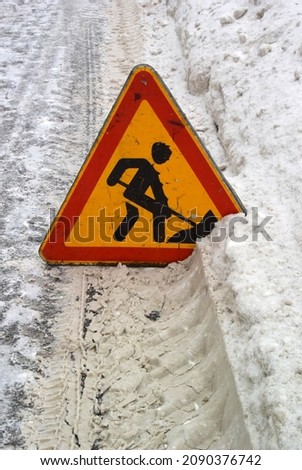Winter photography with a triangular warning road sign in the snow. Renovation work sign. Digging man icon.