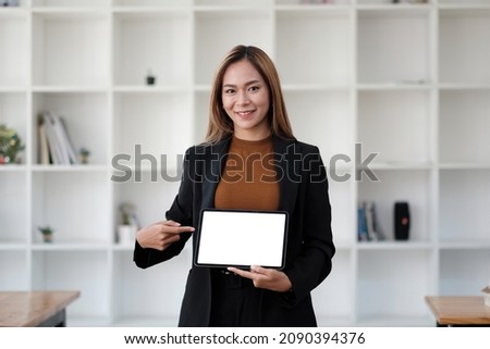 Happy attractive young asian woman displaying a blank white digital tablet blank screen to the camera for your copyspace and text.