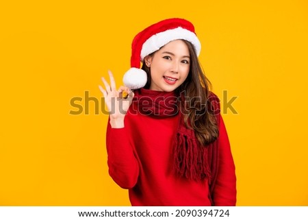 Cheerful young brunette Santa woman in sweater Christmas hat showing OK gesture looking camera isolated on yellow colour background, studio portrait. Happy New Year celebration merry holiday concept
