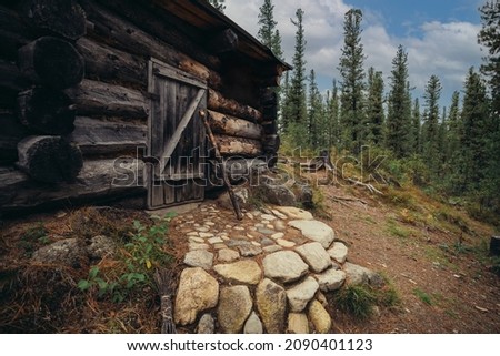 A house made of logs, with stone steps, on top of the hill surrounded by pine trees. An old wooden cabin in a secluded area of the forest. A rustic medieval forester hovel in the middle of nature Royalty-Free Stock Photo #2090401123