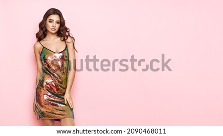 Beautiful woman in cocktail dress posing on pink background. Beauty model with long curly hair. Christmas or New Year festivities. Holiday and Party