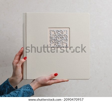 woman holds square wedding photo book with fabric  cover and decor shield close up with copy space for text.
sample beige family photo album in female hands isolated on white background.  photoalbum 