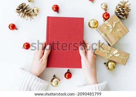 a red book in the hands of a young girl against the background of gifts and Christmas toys. the concept of Christmas. High quality photo
