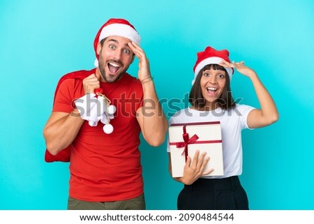 Young couple with christmas hat handing out gifts isolated on blue background has just realized something and has intending the solution