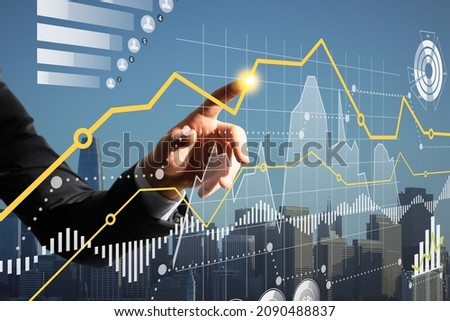 Close up of businessman finger pointing at creative business graph hologram on blurry city grid background. Finance, income and analysis concept. Double exposure