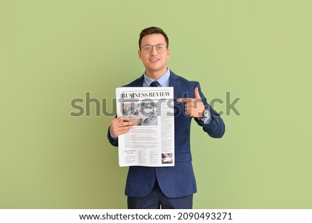 Young businessman pointing at newspaper on color background