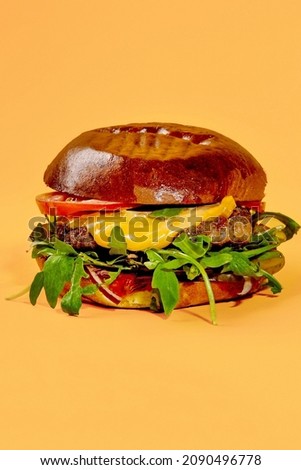 Burger with veal patty, cheese, tomatoes, onion and arugula isolated on pastel orange background