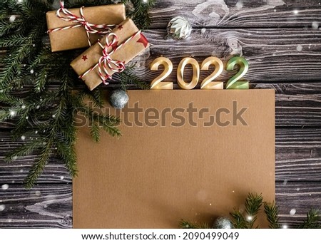 Top view New Year greeting card with copy space. Craft gifts, branches of christmas tree and zirphra 2022 on dark wooden background, flat lay.