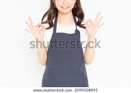 A young girl in an apron standing in front of a white background and posing OK