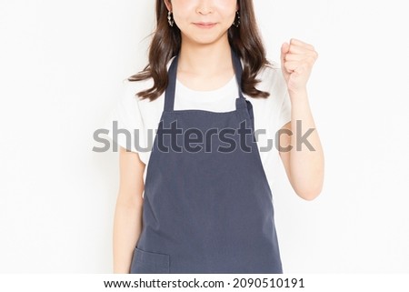 A young girl in an apron standing in front of a white background and doing a guts pose