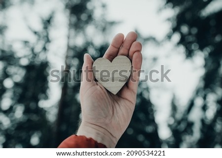 Man palm holding heart on blurred winter forest trees.Valentine's day concept.Toned,copy space.