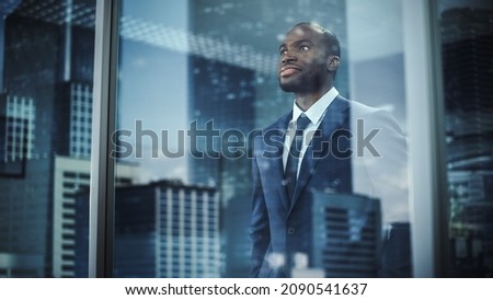 Thoughtful African-American Businessman in a Perfect Tailored Suit Standing in His Office Looking out of the Window on Big City. Successful Investment Manager Planning Strategy. Outside Shot Royalty-Free Stock Photo #2090541637