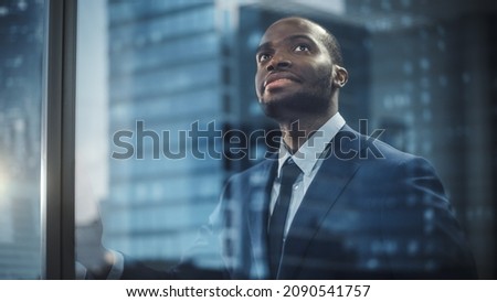 Thoughtful African-American Businessman in a Perfect Tailored Suit Standing in His Office Looking out of the Window on Big City. Successful Investment Manager Planning Strategy. Outside Shot Royalty-Free Stock Photo #2090541757