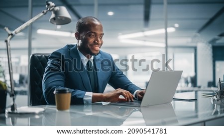 Top Management Modern Office: Successful Black Businessman in Tailored Suit Working on Laptop Computer. Professional African American CEO Managing Investment Strategy. Portrait of Top Manager