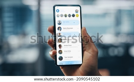 Black Businessman Holding Smartphone with Social Media App in Office. African-American Businessperson using Internet, Social Media with Mobile Phone Device. Over Shoulder Shot Royalty-Free Stock Photo #2090545102