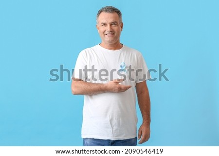 Mature man with blue ribbon on color background. Prostate cancer awareness concept Royalty-Free Stock Photo #2090546419