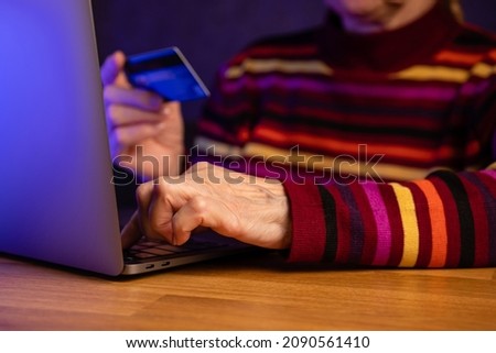Modern elderly retired woman makes purchases online using credit card on laptop at home.