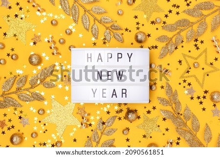 Happy New Year. Lightbox and golden glittering decorations on a yellow background.