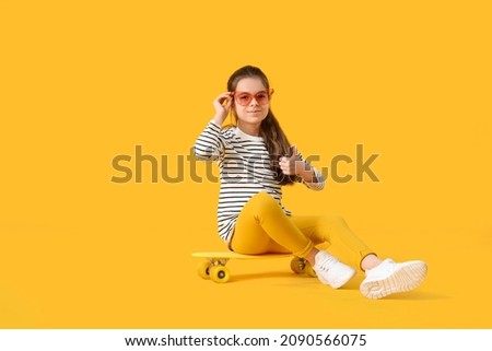Cute little girl with skateboard showing thumb-up gesture on color background