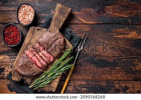 Fried Top Blade or flat iron roast beef meat steaks on wooden board with rosemary. Dark wooden background. Top View. Copy space Royalty-Free Stock Photo #2090568268