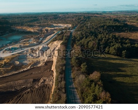 Ariel photograph of Bovington, Dorset showcasing greenery on one side of the road and quarry works on the other.
