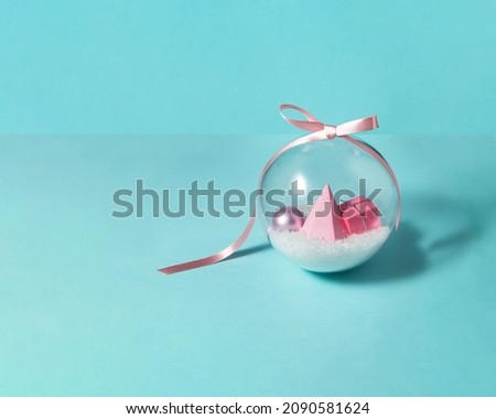 Snow, pastel pink Christmas tree and decoration in transparent Xmas bauble with satin bow on light blue background. Minimalistic New Year composition. Creative Winter holidays concept.