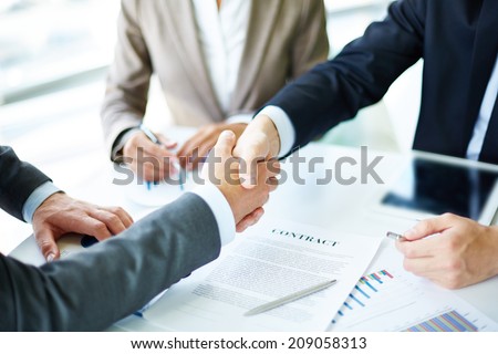 Image of business partners handshaking over business objects on workplace Royalty-Free Stock Photo #209058313