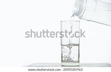 Pouring water from a pitcher to a glass set on a wooden bar on a white background.