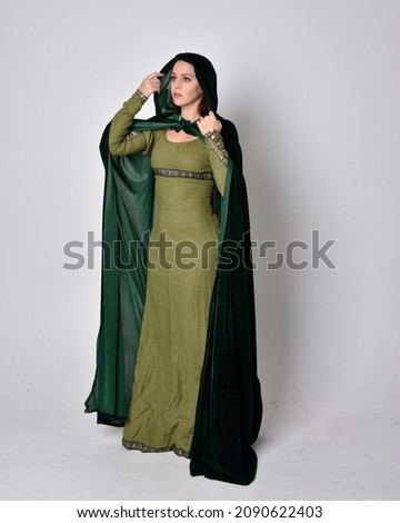 Full length portrait of red head girl wearing  green Celtic medieval gown and velvet cloak. Standing  pose with gestural hands.  isolated on  studio background 