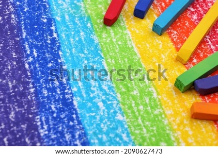 Colorful pastel chalks on drawing of rainbow. Space for text