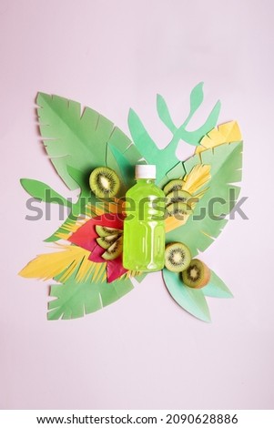 green kiwi juice in a bottle with paper leaves on a pink background
